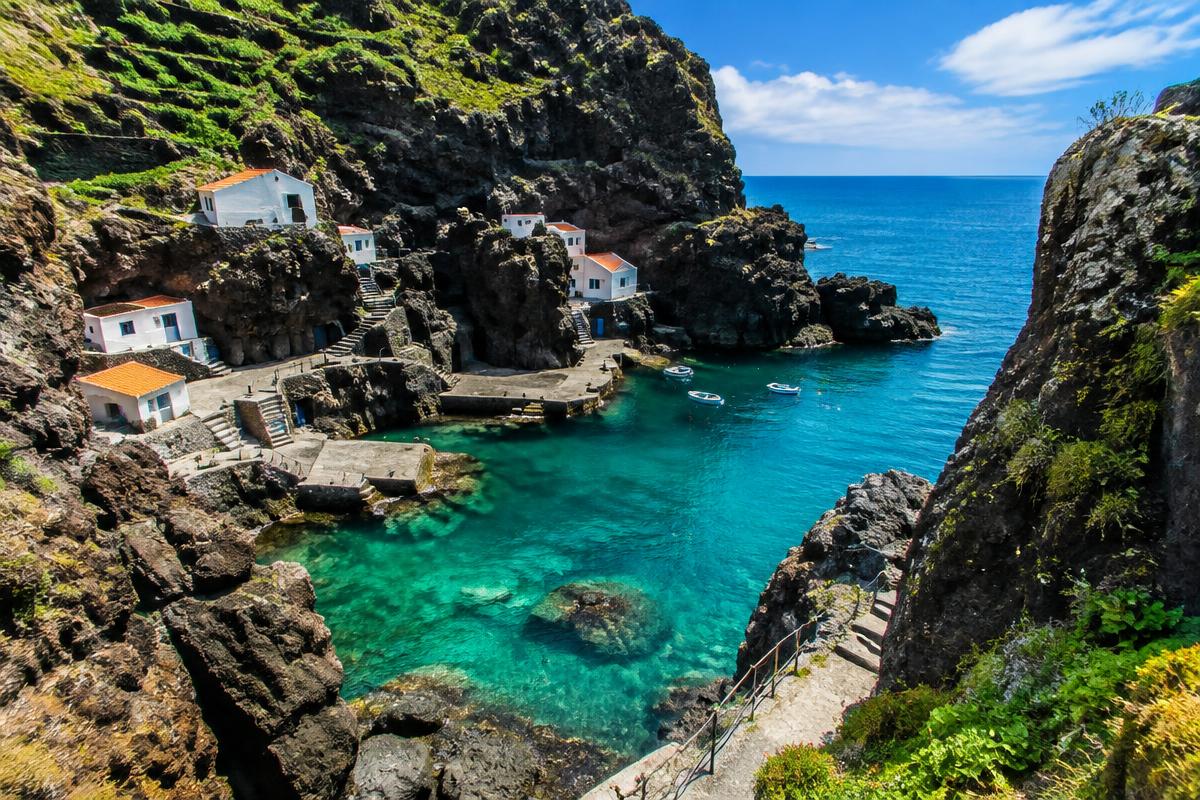 Cala escondida con casas blancas encajadas en un acantilado de roca volcánica y agua turquesa